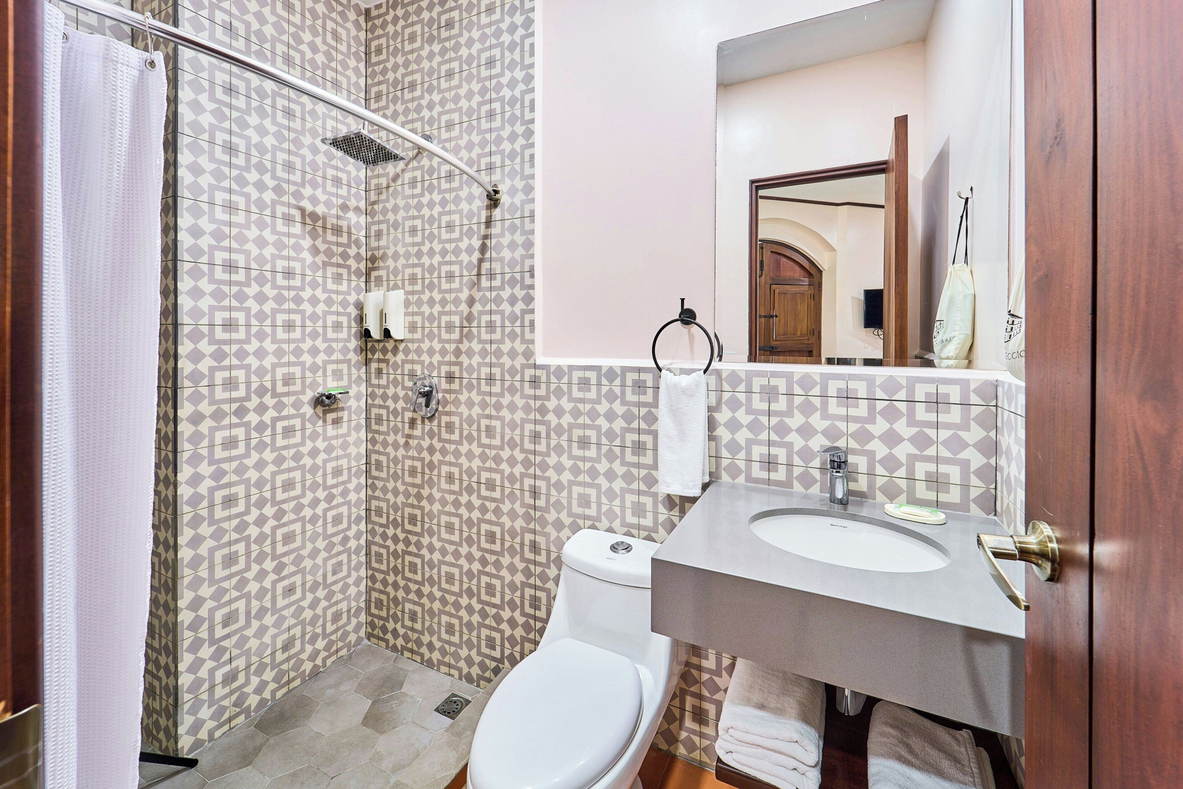 A bathroom with a shower, toilet, sink, and a mirror.