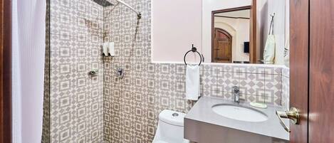 A bathroom with a shower, toilet, sink, and a mirror.