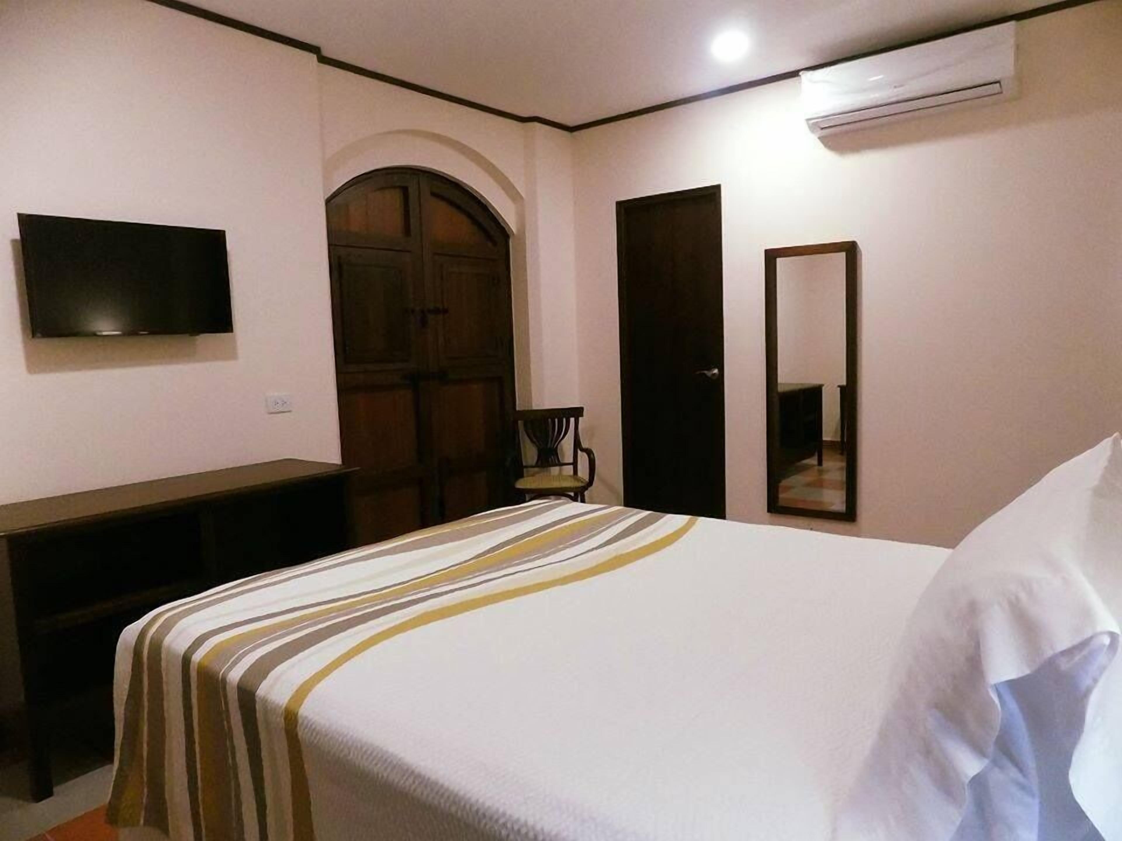 Un dormitorio con cama, televisión montada en la pared, escritorio y armario.