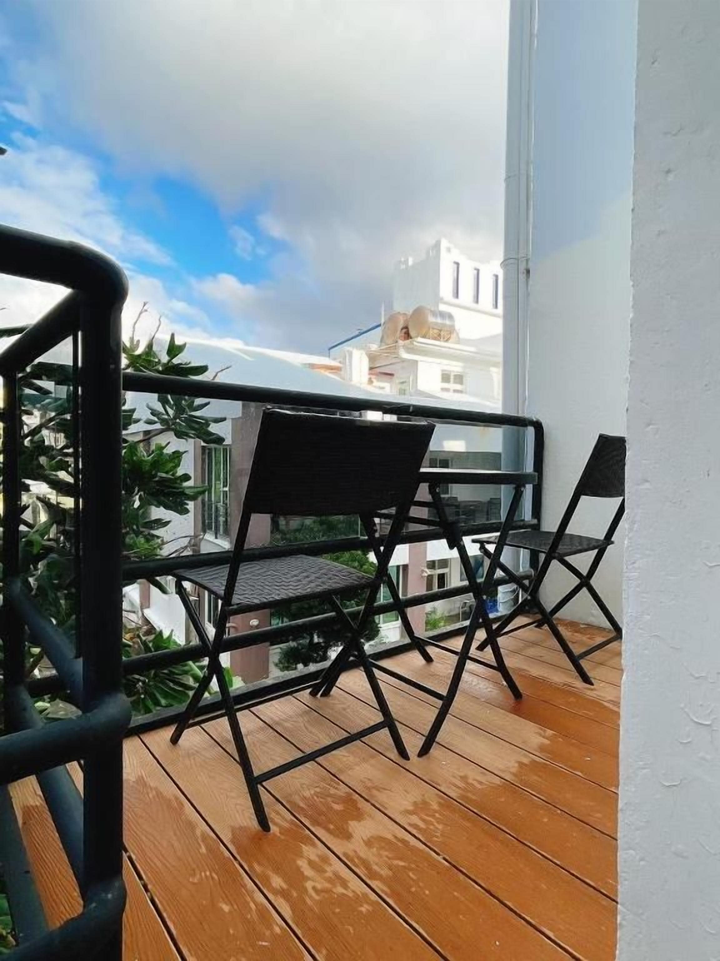 A balcony with a wooden floor and two black chairs.