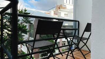 A balcony with a wooden floor and two black chairs.