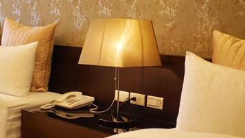 Habitación de hotel con cama, mesita de noche con lámpara, teléfono e enchufe.
