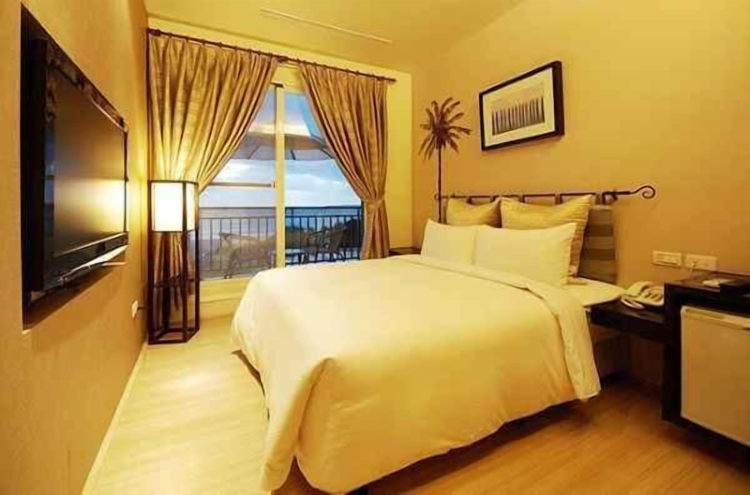 A hotel room with a bed, a desk, a lamp, a TV, and a balcony view.