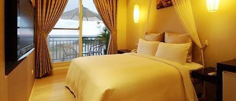 A hotel room with a large bed, a TV, a desk, and a balcony with curtains.