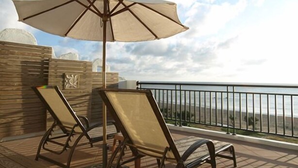 Un balcon avec deux fauteuils et un grand parasol, donnant sur une zone côtière.