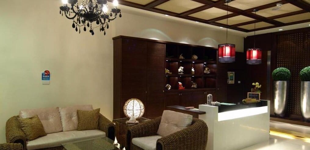 Una sala de estar moderna con un sofá, una mesa de centro y una lámpara decorativa. Hay un mueble de madera con estantes y un pequeño mostrador de recepción.