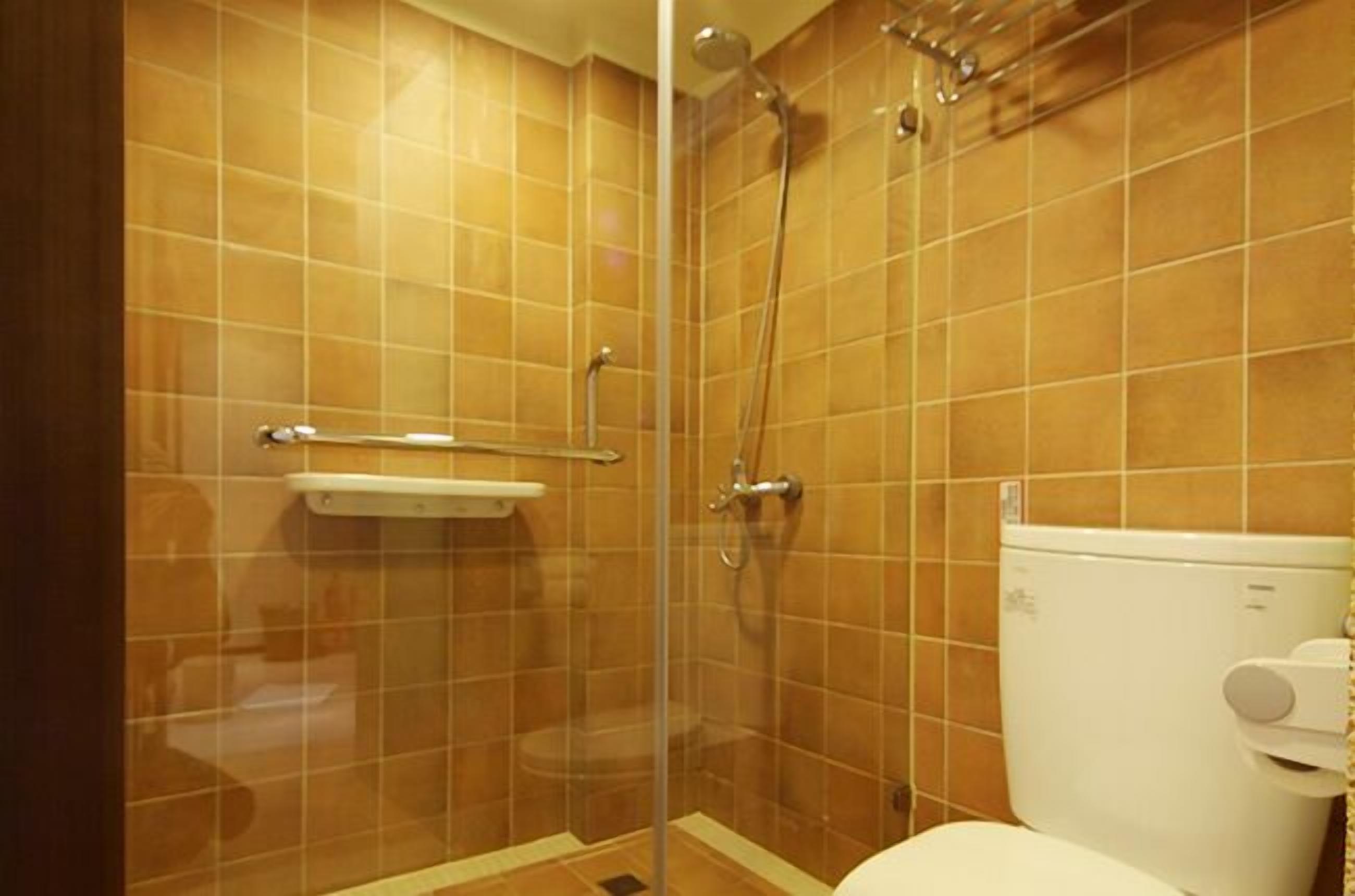 A bathroom with a glass-enclosed shower, a white toilet, and a shelf above the toilet.