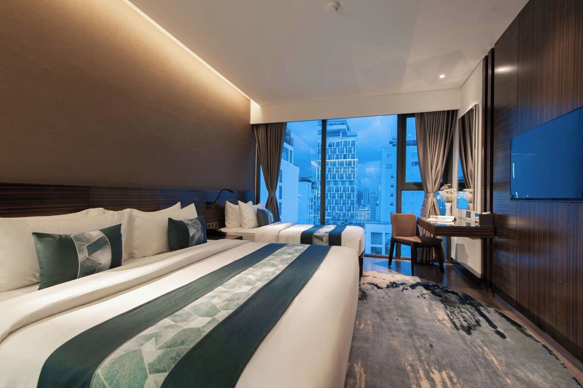 A hotel room with a large bed, a desk, and a view of the cityscape.