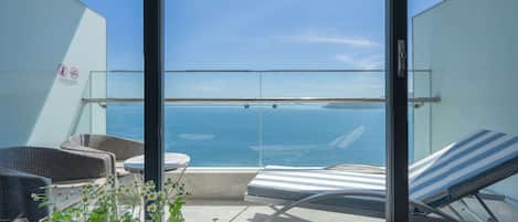 Un balcón con dos sillones de descanso, una mesita y baranda de cristal con vista al mar.