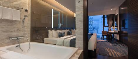 Une chambre d’hôtel moderne dotée d’une grande baignoire, d’une chambre séparée avec un lit et une vue sur la ville, ainsi que d’un coin repas avec une table et des chaises.