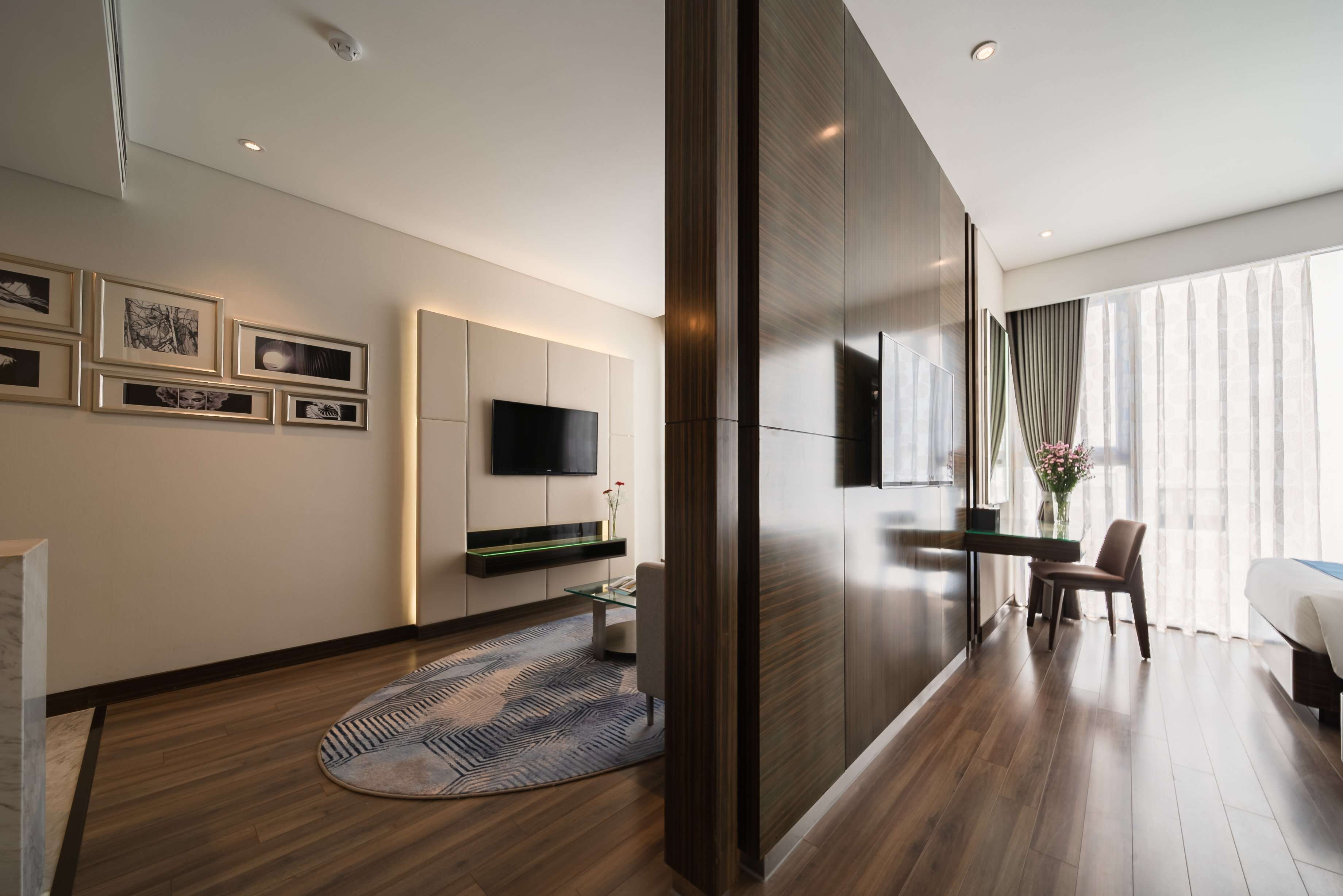 A modern living room with a flat-screen TV, a glass coffee table, a sofa, and a large window with curtains.