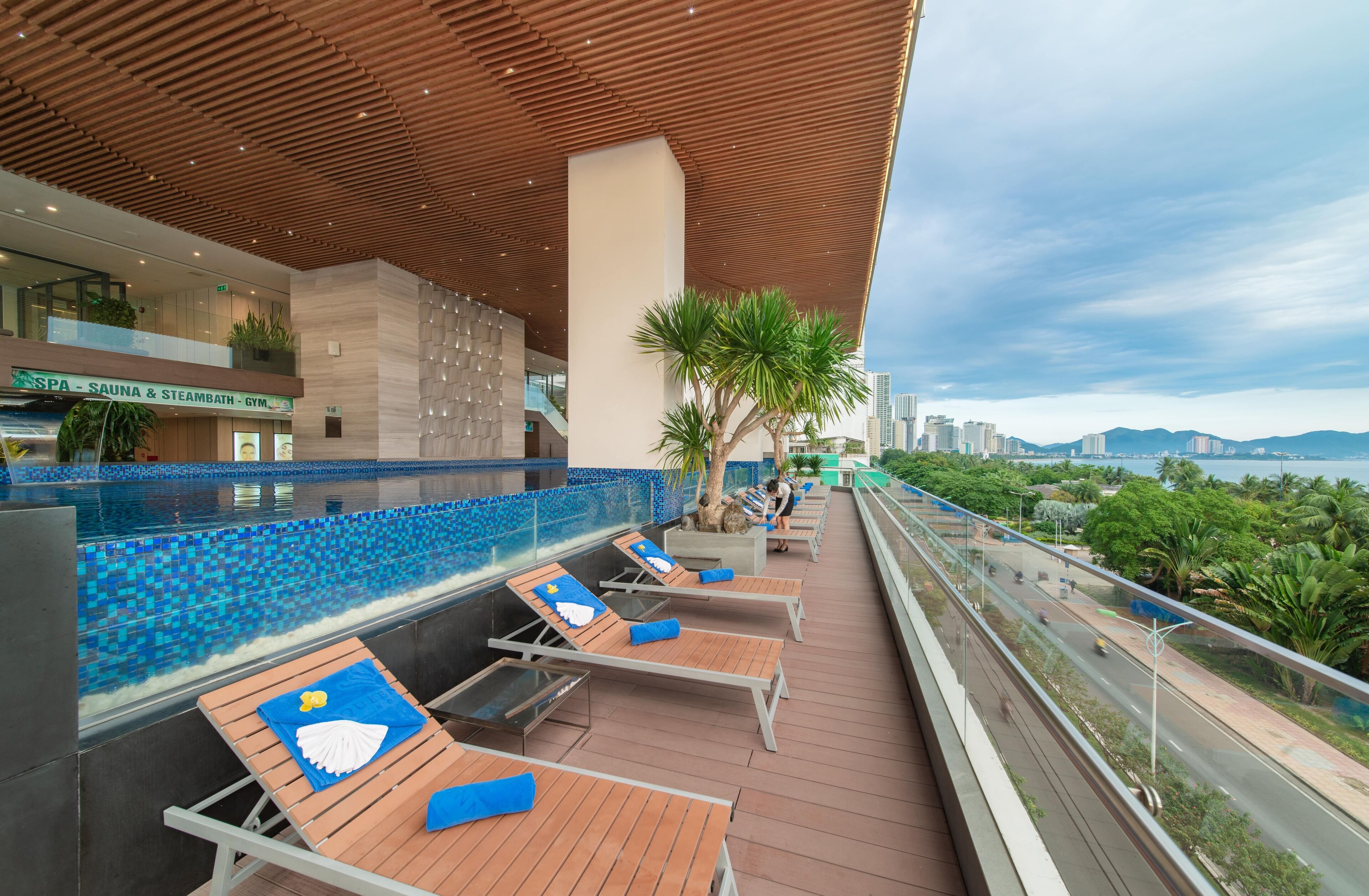 A rooftop lounge with sun loungers, a pool, and a view of the city skyline.