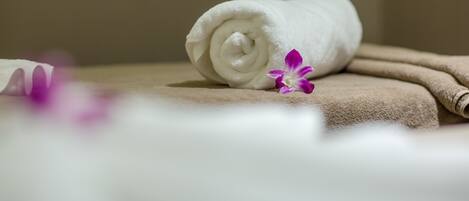 A rolled white towel and a purple flower on a beige surface.