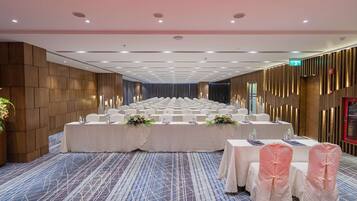 A conference room with rows of tables and chairs, a stage, and a blue carpet.