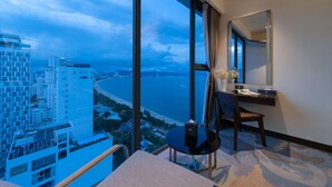 A hotel room with a large window offering a city view, a small round table, a chair, and a desk with a mirror. - Queen Ann Nha Trang (Nha Trang)
