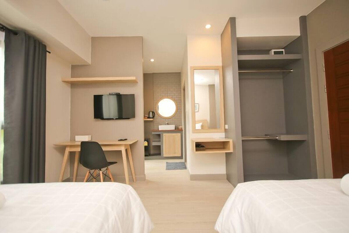 Ein Hotelzimmer mit zwei Betten, einem Schreibtisch, einem Fernseher, einem Spiegel und einer Dusche.