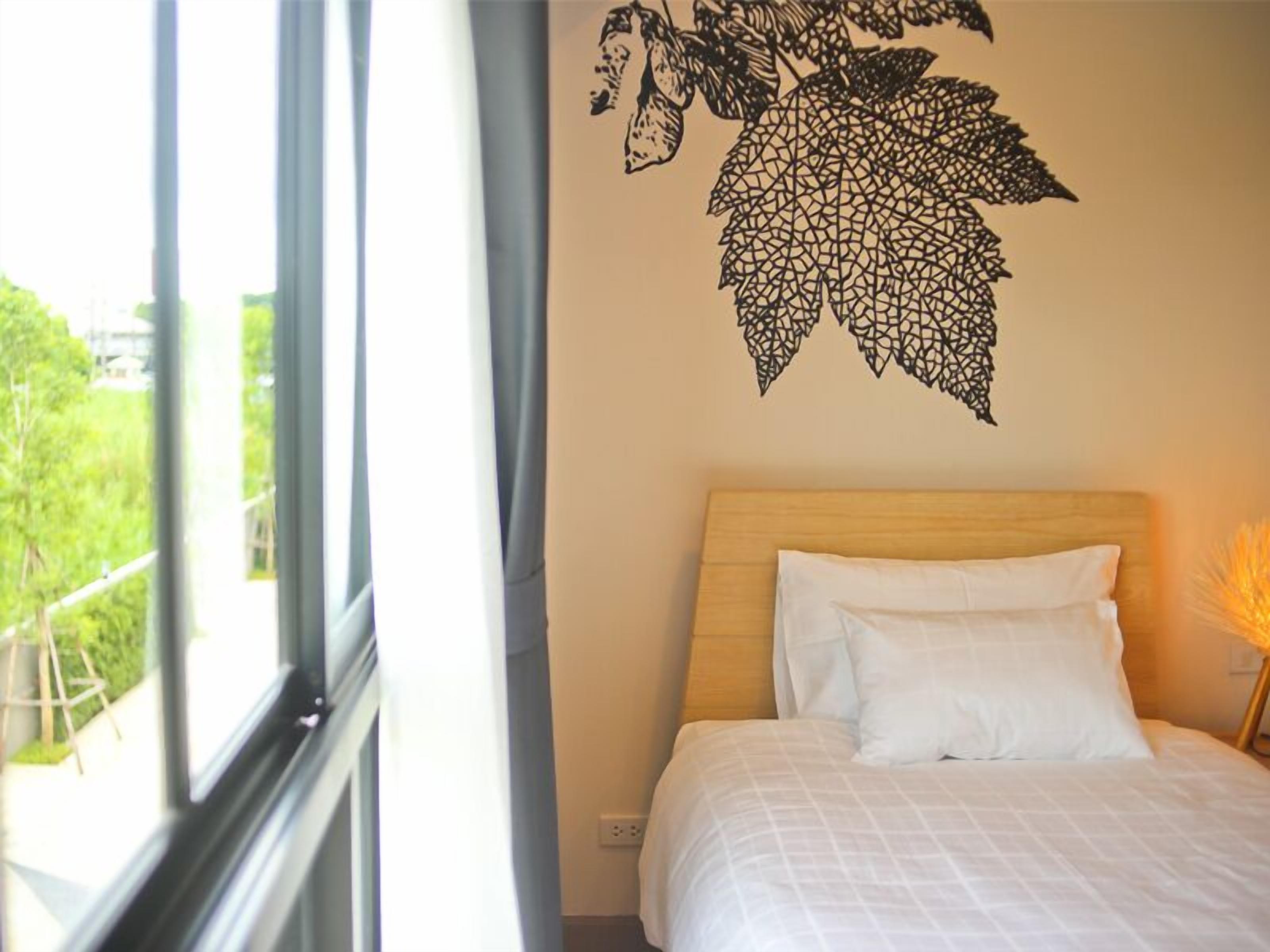 A bedroom with a bed, a window, and a wall decoration of leaves.