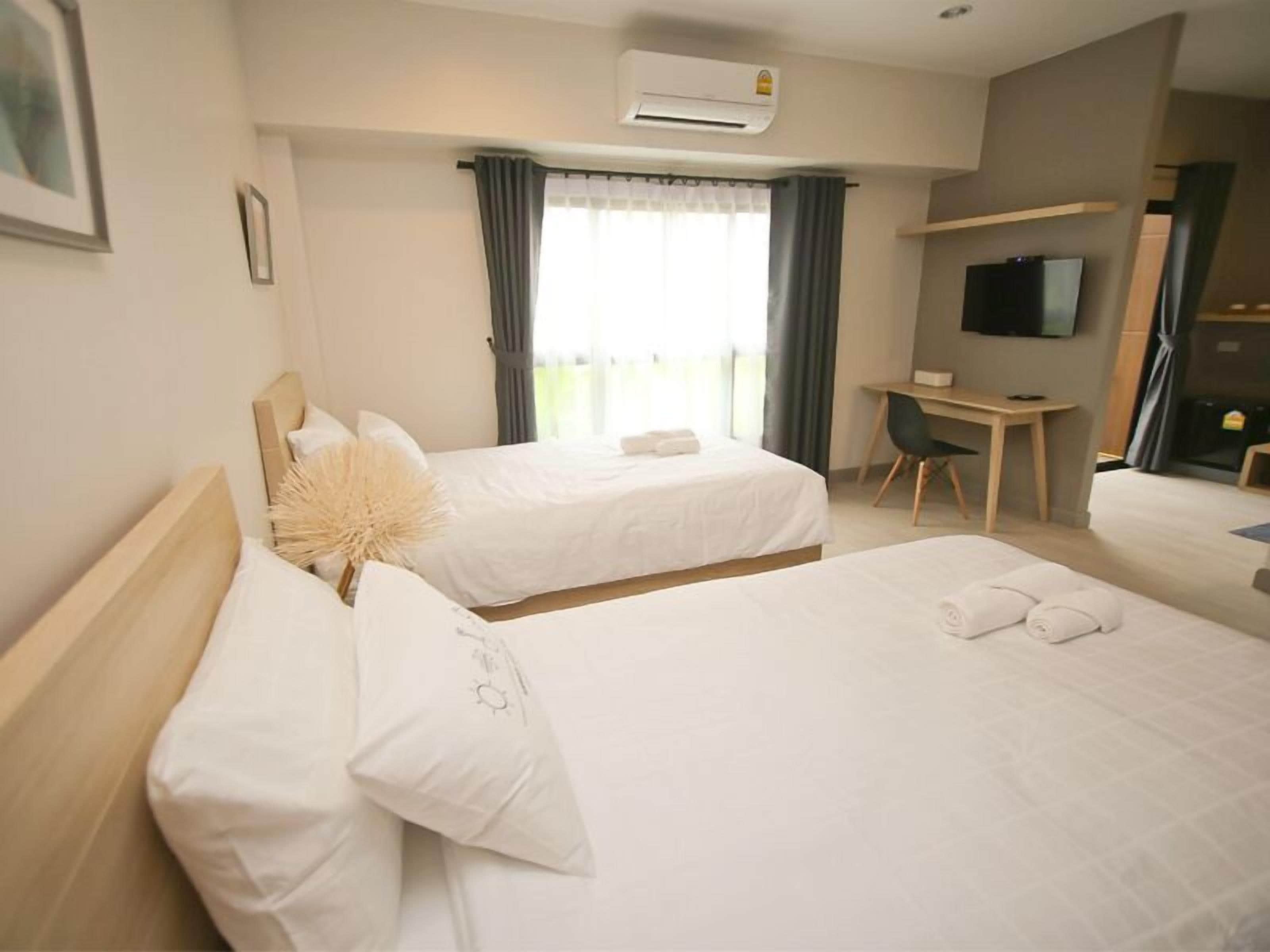 A hotel room with two beds, a desk, a TV, and an air conditioning unit.