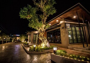 A modern building with a cafe sign, a tree with lights, and a paved entrance.