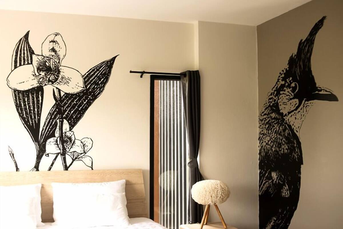 Ein Schlafzimmer mit Bett, Wandvorhang und einem Wandbild von einem Vogel.