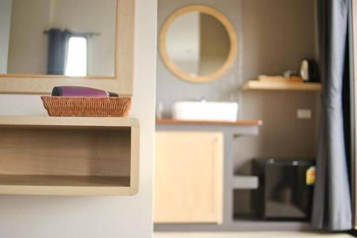 Ein Badezimmer mit Holzregal, einem Korbwäscher und einem runden Spiegel.