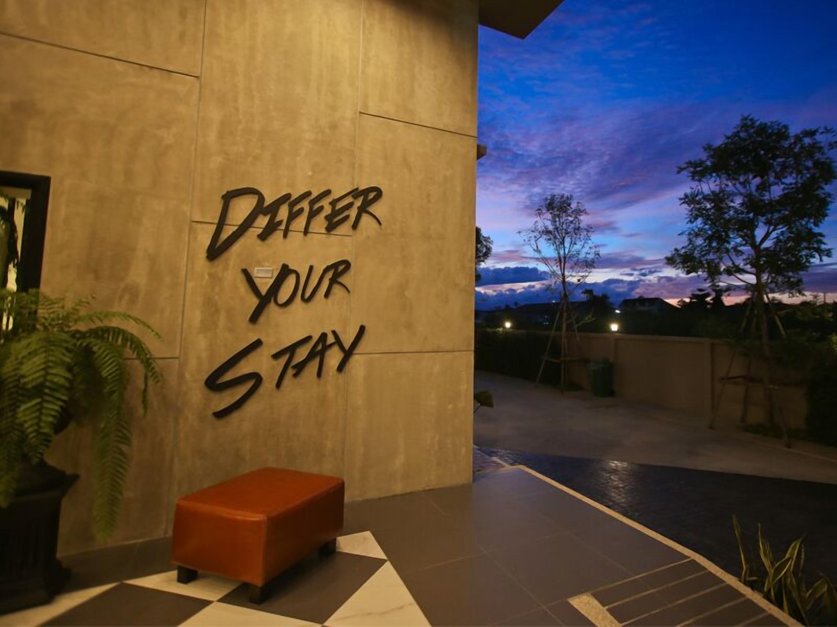 A modern building exterior with a motivational phrase "Dare your stay" on the wall, a small orange bench, and a view of the sky at dusk.