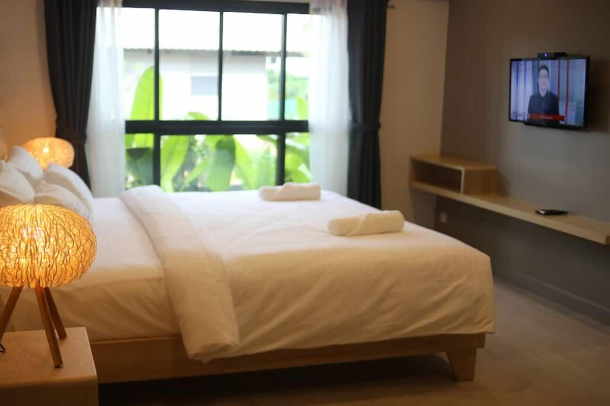 Ein Hotelzimmer mit Bett, Nachttischlampe, Fernseher an der Wand und einem Fenster mit Blick ins Grüne.