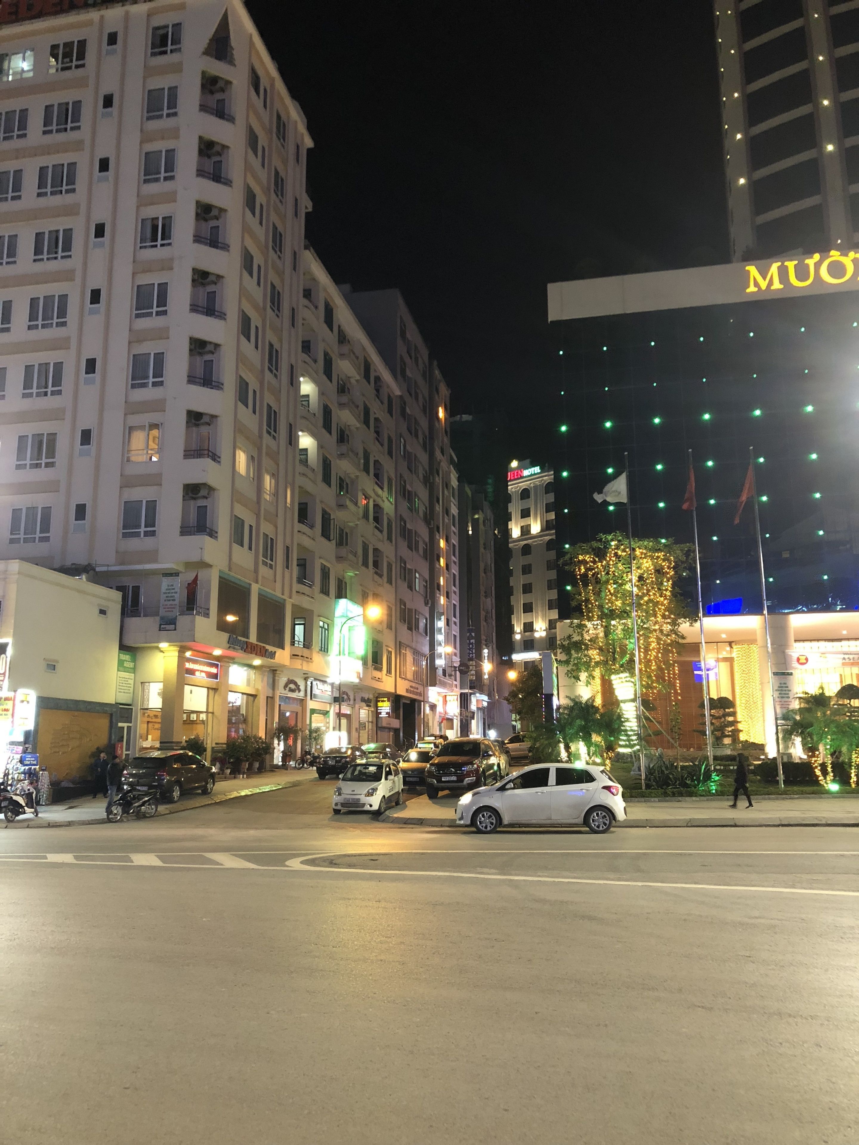 A multi-story hotel with a prominent 'MUON' sign, a visible entrance, and a well-lit street with parked cars and pedestrians.