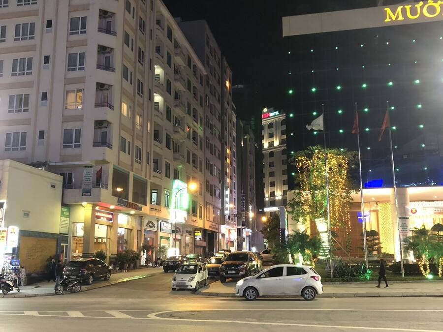 A multi-story hotel with a prominent 'MUON' sign, a visible entrance, and a well-lit street with parked cars and pedestrians.