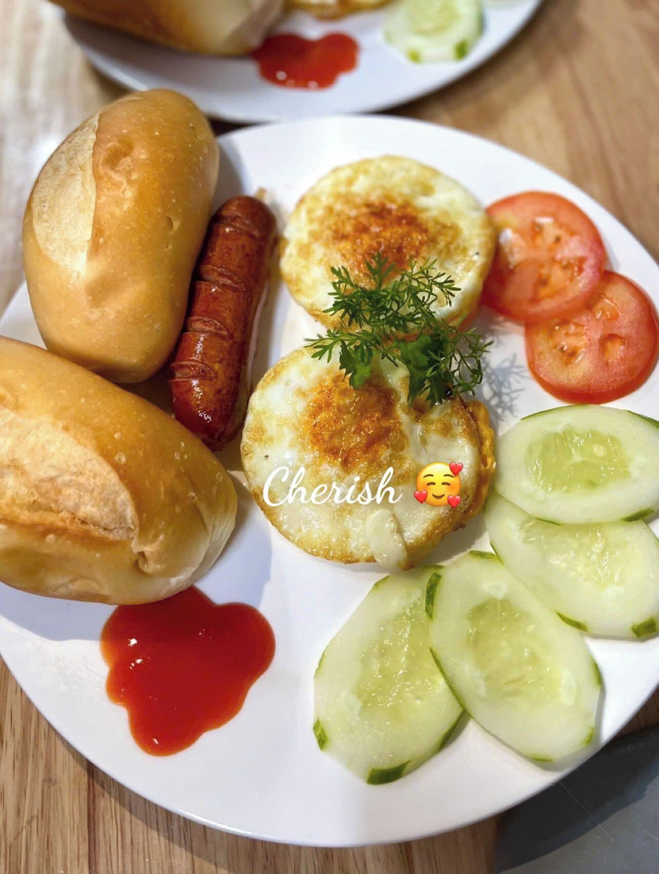 A plate of food including sausages, bread rolls, and sliced cucumbers with a garnish.