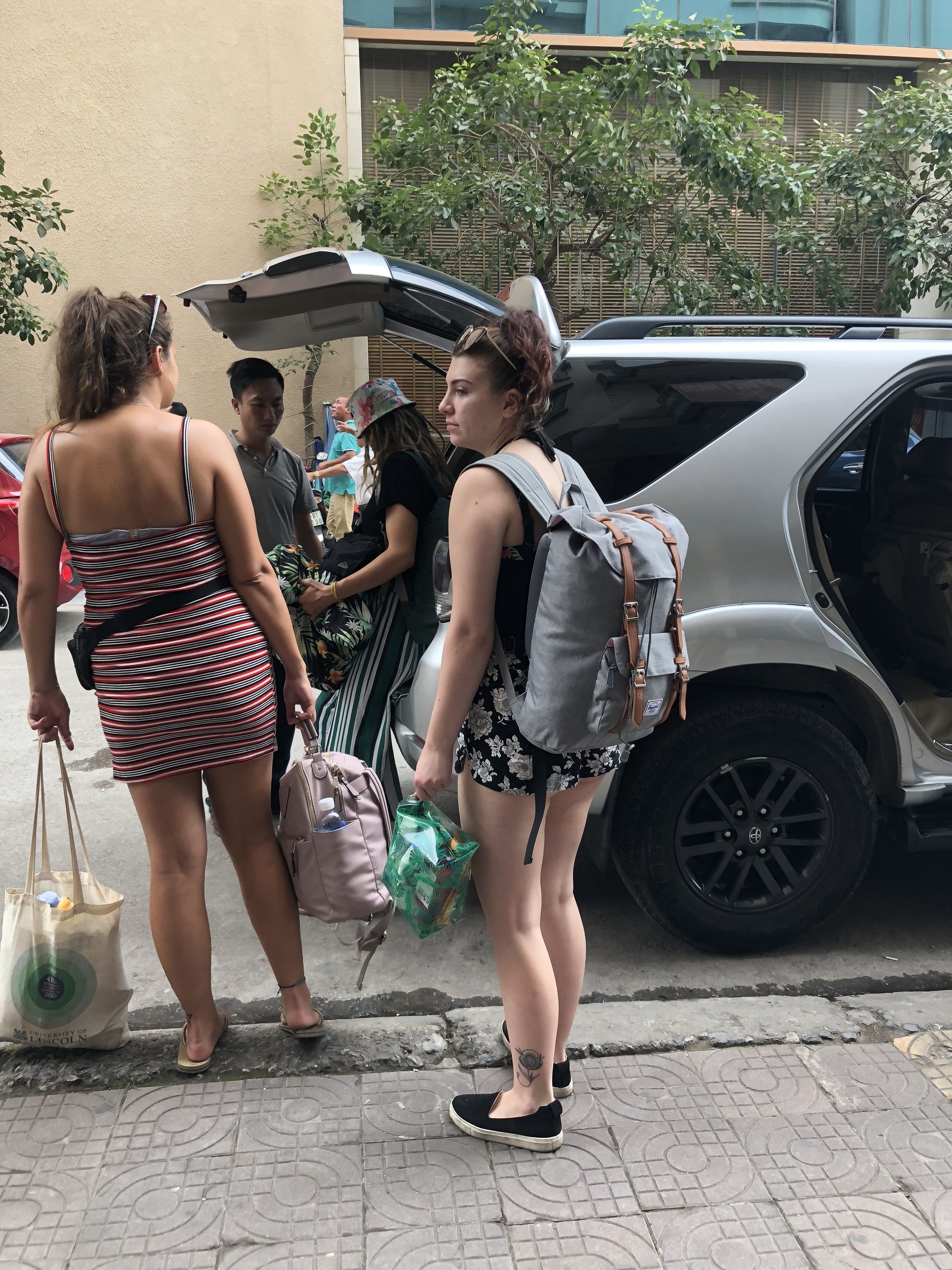 Un grupo de personas de pie cerca de un coche estacionado en una calle pavimentada.