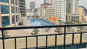 Vue d’une piscine et de ses abords, avec les bâtiments environnants, notamment un grand hôtel et des immeubles d’habitation.
