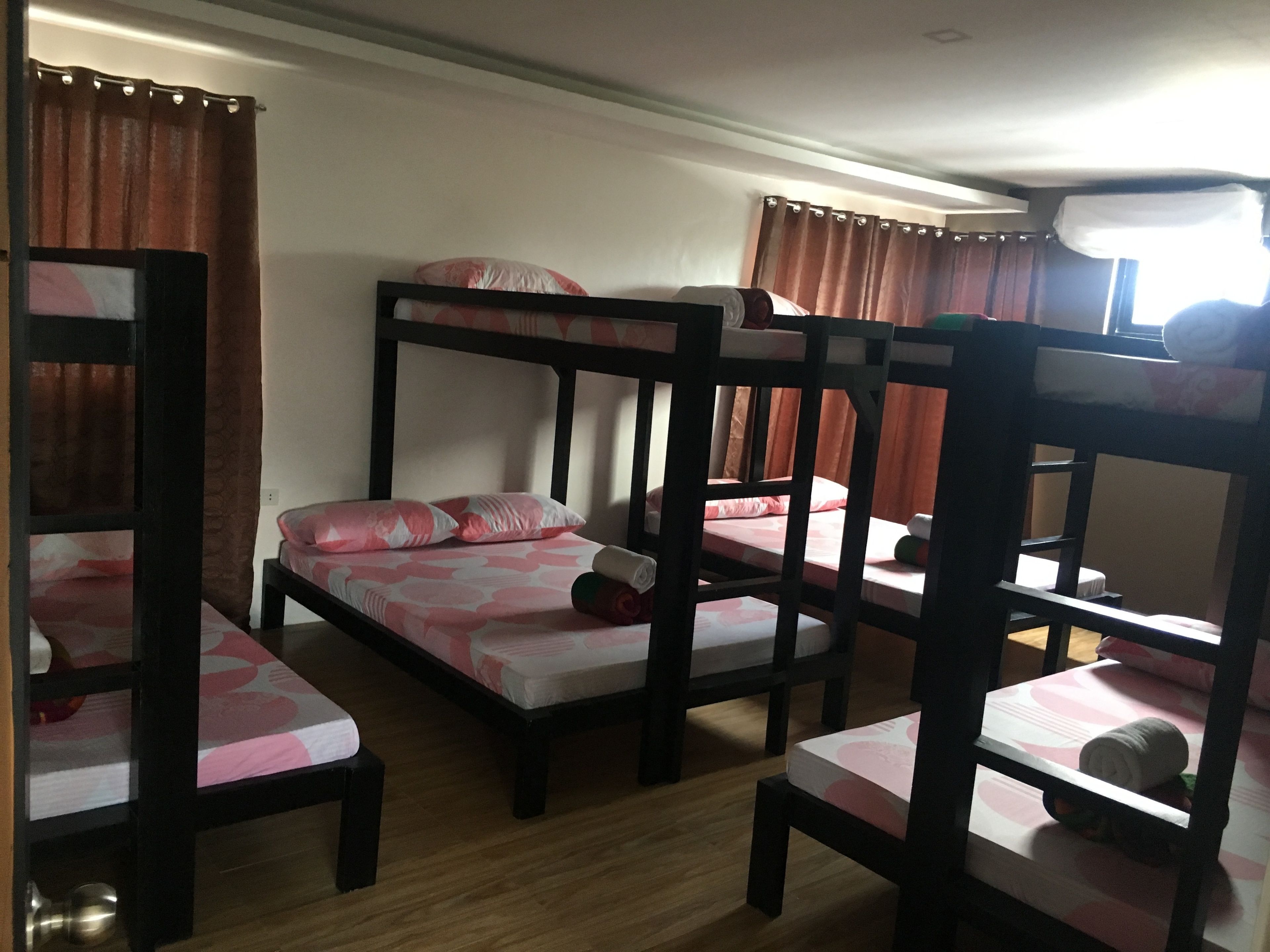 A room with bunk beds and a single bed, wooden floors, and curtains.