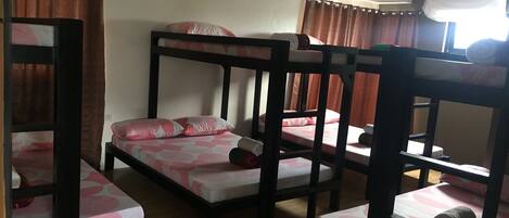 A room with bunk beds and a single bed, wooden floors, and curtains.