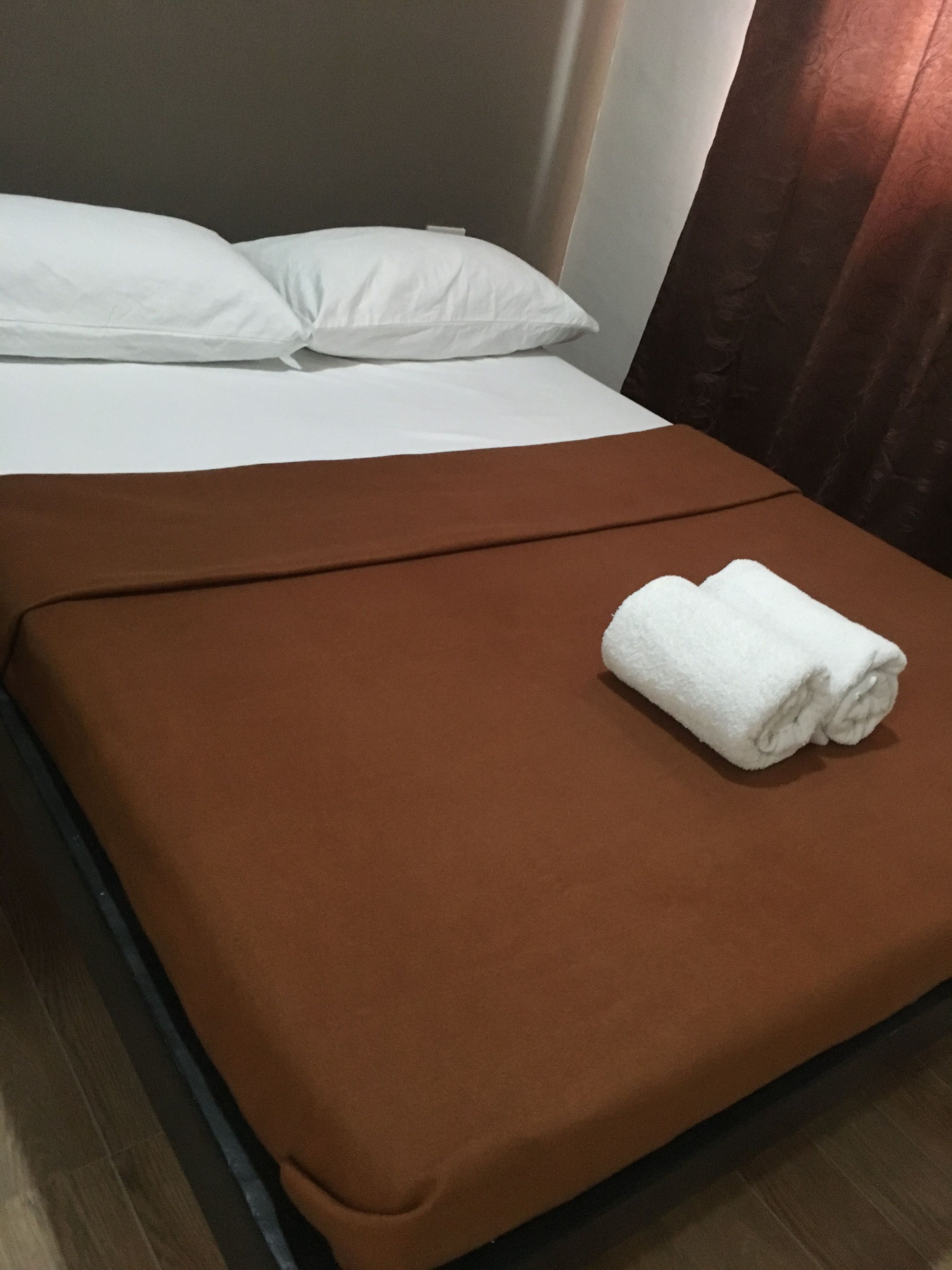 Un lit bien fait, avec des draps blancs et une couverture marron.