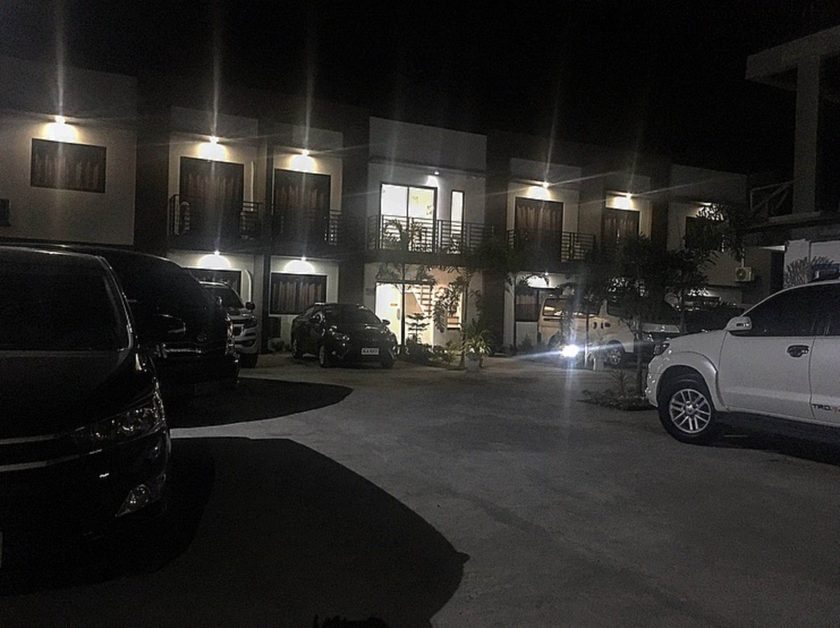 Un estacionamiento con varios coches aparcados frente a un edificio con múltiples balcones y ventanas iluminadas.