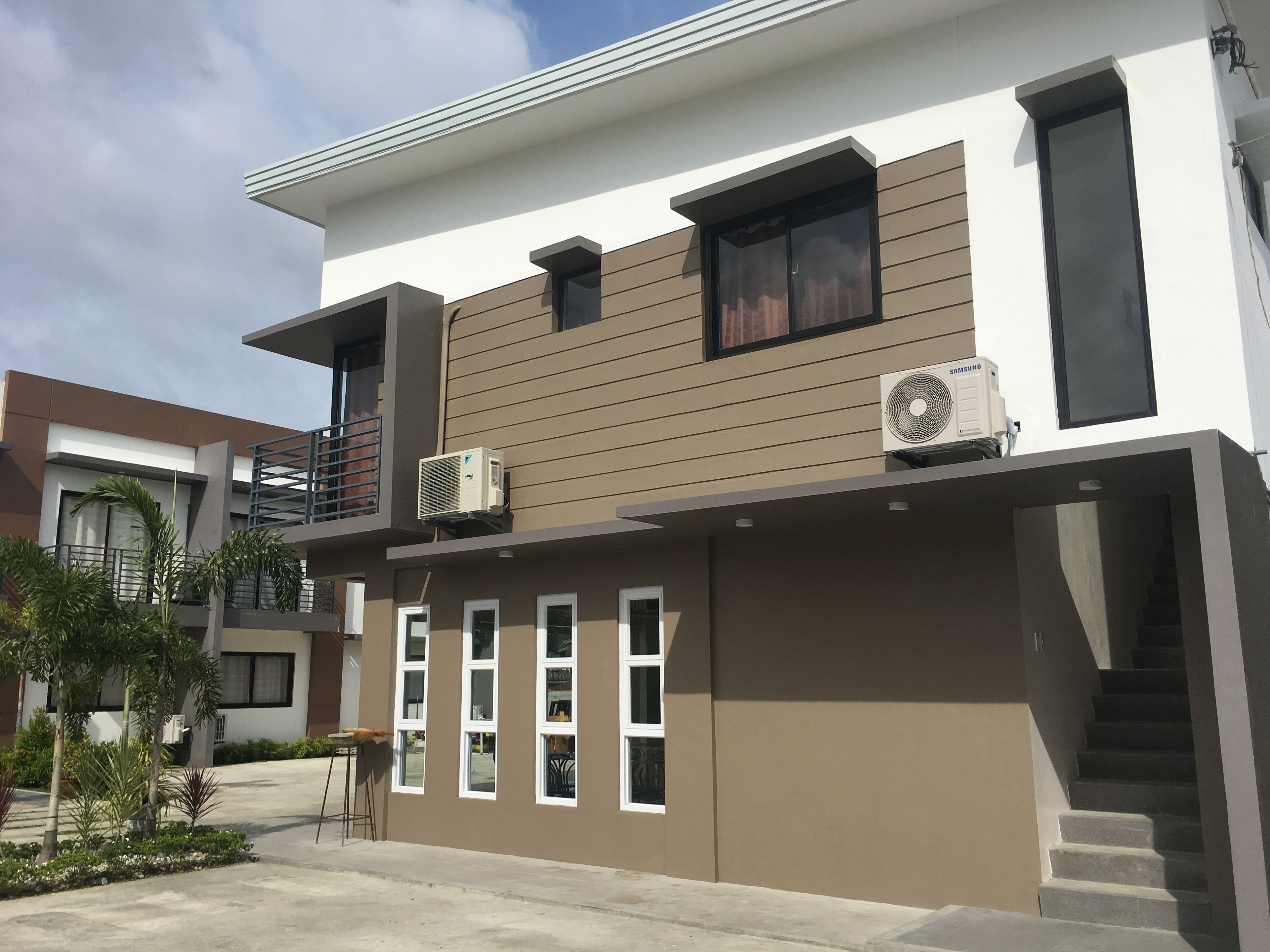 A modern two-story residential building with a flat roof, large windows, and air conditioning units.