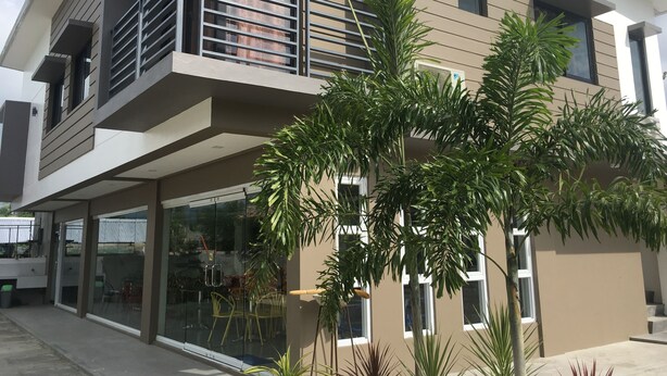 A modern two-story building with a balcony, large windows, and potted plants.