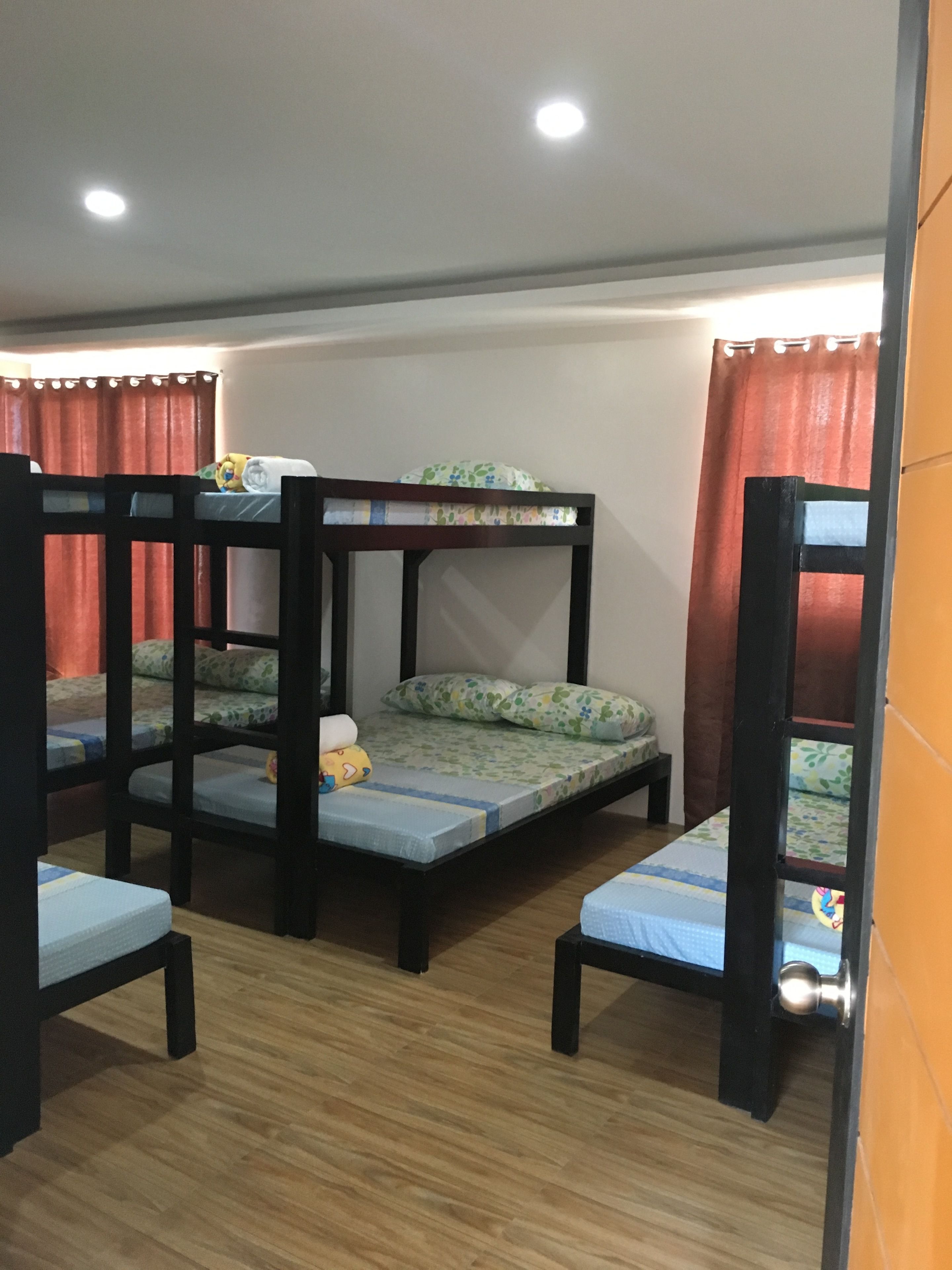 A room with bunk beds, wooden flooring, and a curtain.