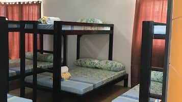 A room with bunk beds, wooden flooring, and a curtain.