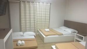 A hotel room with two single beds, a large window with a curtain, and a wooden floor.