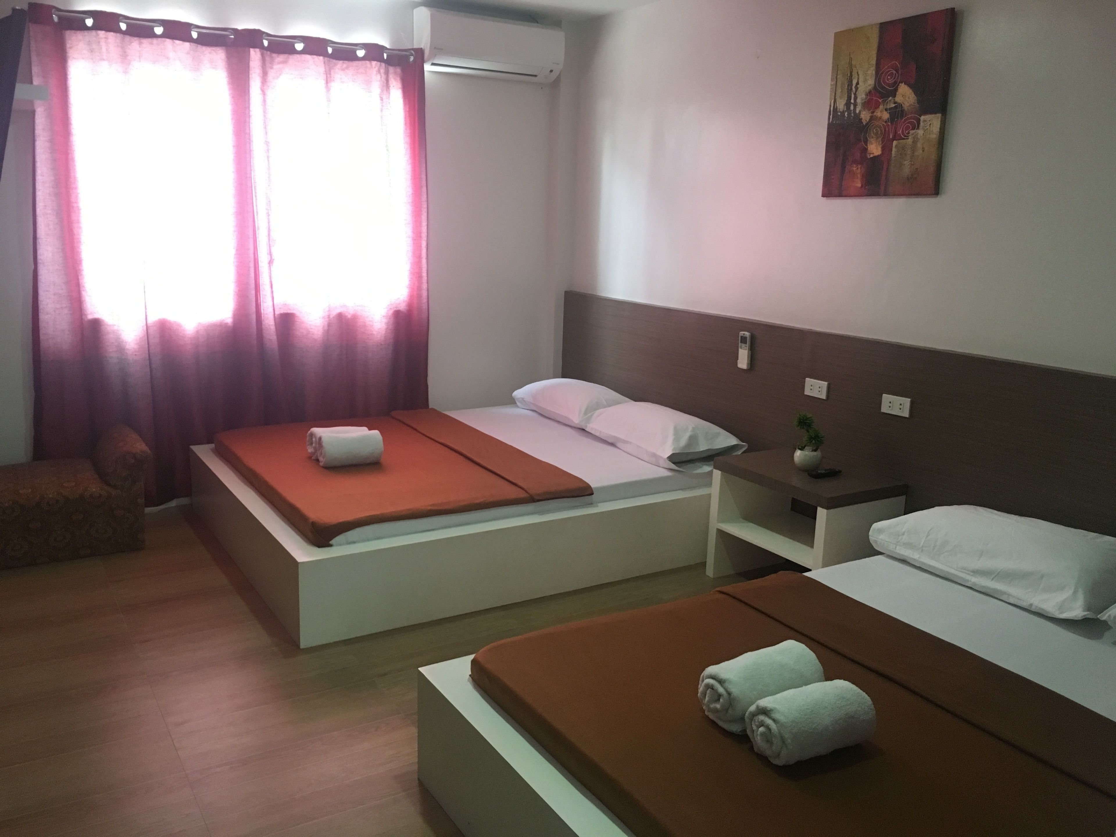 Una habitación de hotel con dos camas, una mesita de noche con una planta, una pequeña silla y un cuadro en la pared.