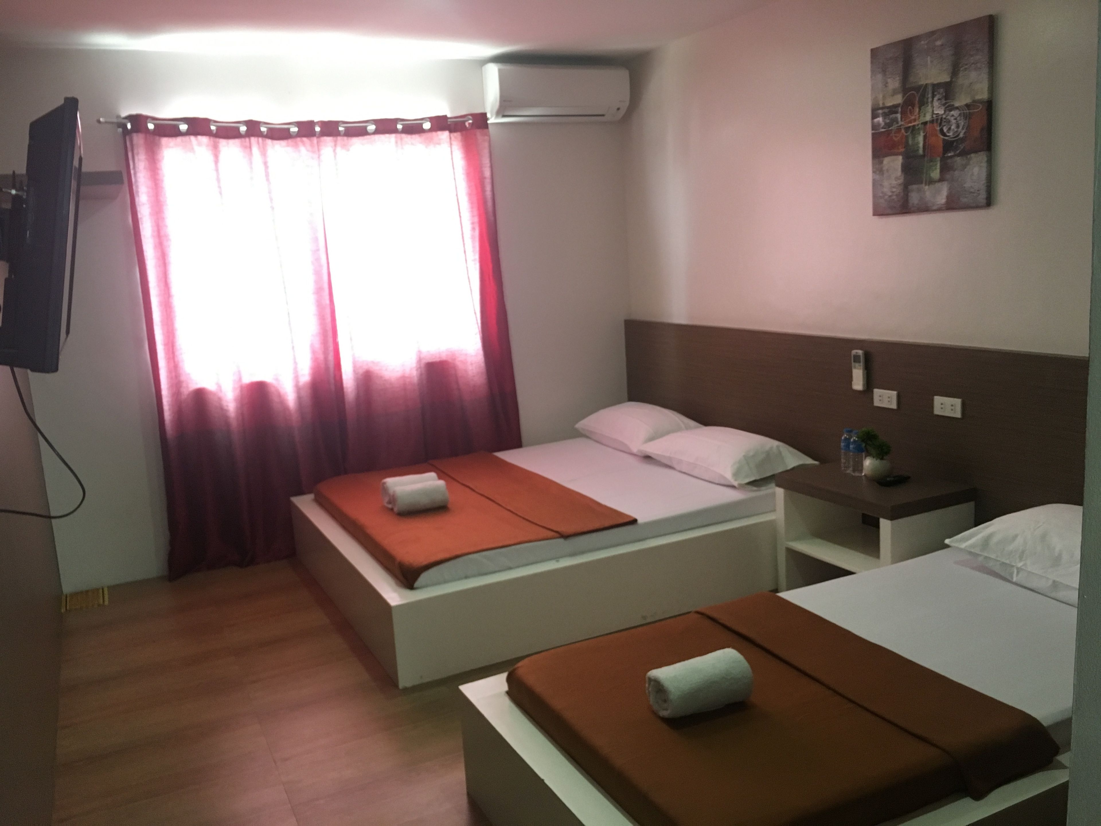 A hotel room with two beds, a TV, an air conditioner, and a painting on the wall.