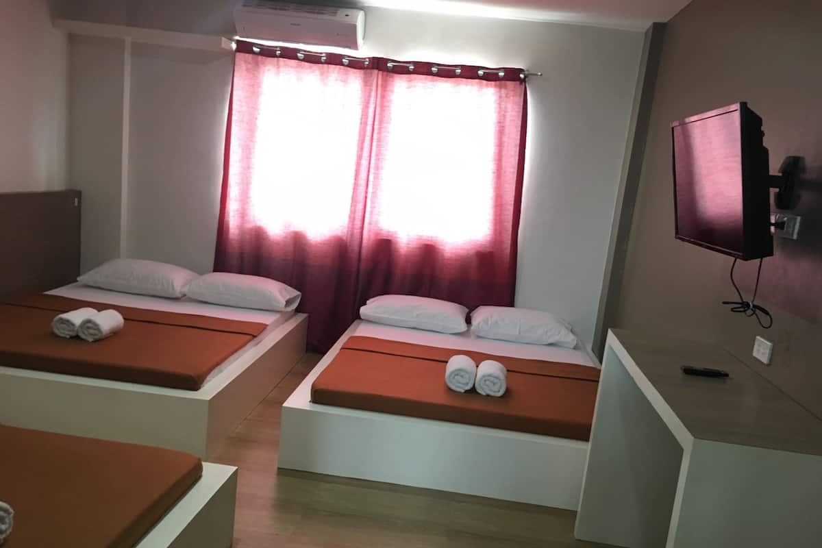 A hotel room with two single beds, a TV on the wall, and a window with curtains.