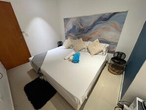 Una cama bien hecha con almohadas, una toalla enrollada y un tapete negro en el suelo.