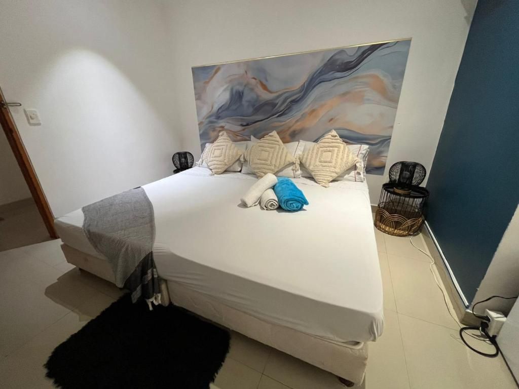 Een slaapkamer met een bed, kussens, een deken, een zwart vloerkleed, een kunstwerk aan de muur en een stoel.