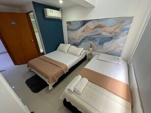 A hotel room with two beds, a large abstract painting on the wall, a door with a number, and an air conditioning unit.