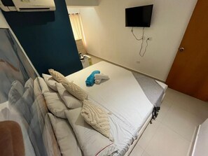 A hotel room with a bed, a television mounted on the wall, and an air conditioning unit.