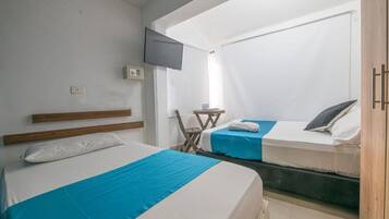 Een kamer met twee bedden, een aan de muur bevestigde televisie, een klein tafeltje en een raam.