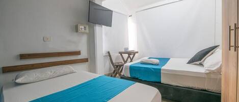 A room with two beds, a TV mounted on the wall, a small table, and a window.